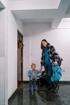 Smiling mother holding the hand of a little girl standing with a stroller in front of the door of the apartment. High quality photo