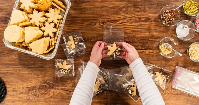 Carefully packaging Christmas cutout cookies, half-dipped in chocolate, sprinkled with crushed nuts, and presented in clear cellophane wrapping.