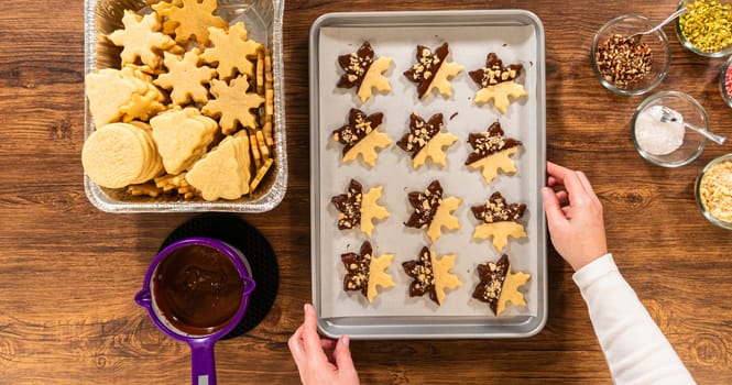 Creating cutout sugar cookies, partially dipped in chocolate and topped with hazelnut pieces, placed on parchment paper.