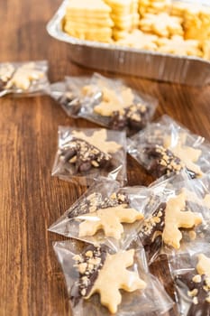 Carefully packaging Christmas cutout cookies, half-dipped in chocolate and presented in clear cellophane wrapping, perfect for festive gifting.