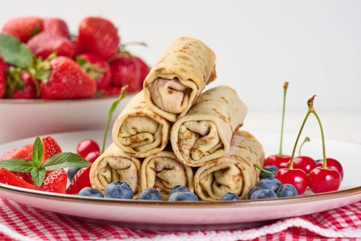 Stack of fried crepes with filling on a round plate, white table