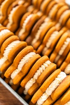 Making gingerbread man cookie sandwiches filled with eggnog buttercream, arrayed on a rustic wooden table, ideal for heartfelt Christmas gifting.