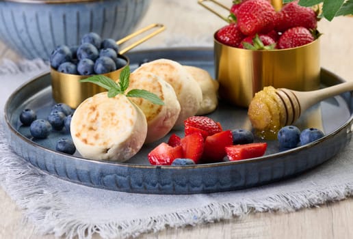 Round small fried cheesecakes on a blue plate with berries. Healthy breakfast