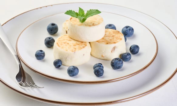 Round small fried cheesecakes on a plate with blueberries. Background white