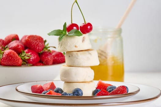 A stack of four cheesecakes on a plate with berries, blueberries, strawberries and cherries. Background white