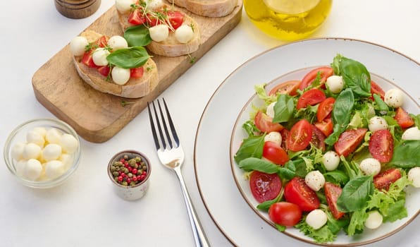 Salad with mozzarella, cherry tomatoes and green lettuce in a white round plate on the table