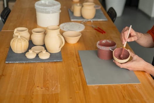 Close-up of a potter's hands with a brush painting ceramic dishes