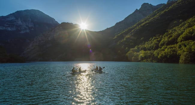 A group of friends enjoying fun and kayaking exploring the calm river, surrounding forest and large natural river canyons during an idyllic sunset