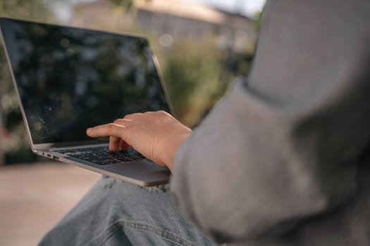 A person is sitting on a bench with a laptop open in front of them. They are typing on the keyboard, possibly working or browsing the internet. Concept of productivity and focus