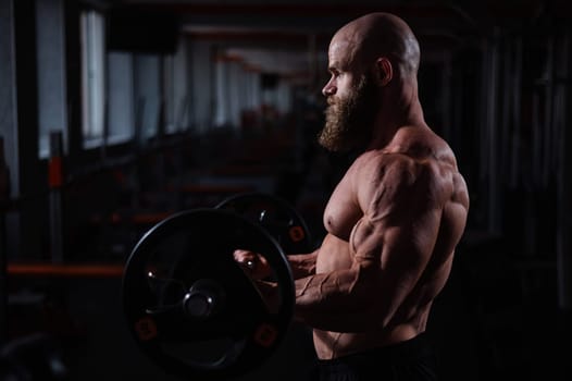 Caucasian bald topless man doing an exercise with a barbell in the gym. Bicep curls with weights