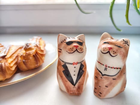 Delectable Dessert Pastries With Charming Porcelain Cat Figurines. Piped cakes sprinkled with sugar beside whimsical cat ornaments