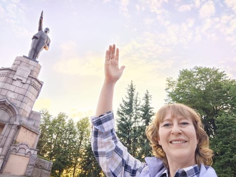Kostroma, Russia - July 04, 2023: A woman poses cheerfully by a Lenin statue, enjoying her travel adventure in a scenic park setting