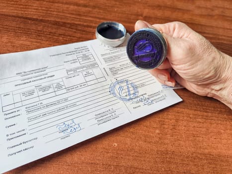 Kirov, Russia - March 18, 2024: Close-up of hand pressing a seal onto paper. Woman Applying Seal to Official Document on Table