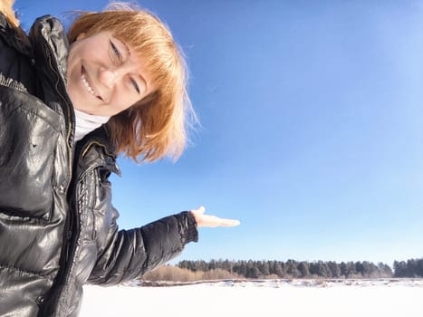 A cheerful middle aged woman in a winter coat taking selfie on nature outdoors in sunny day with blue sky