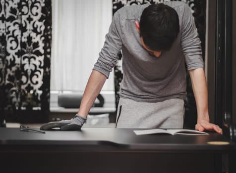 One Caucasian young man in gray clothes stands at a black table with his hands on it and reads instructions for assembling furniture during the day in a room against the background of a window, close-up side view with depth of field. Furniture assembly concept, assembly services.
