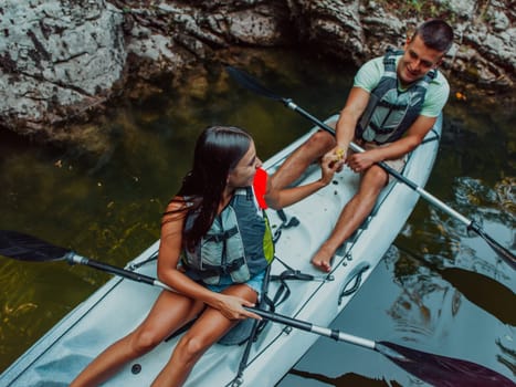 A young couple enjoying an idyllic kayak ride in the middle of a beautiful river surrounded by forest greenery.