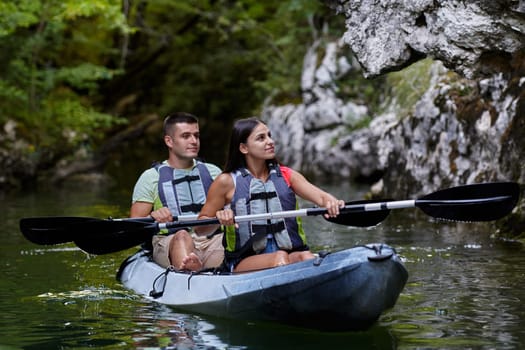 A young couple enjoying an idyllic kayak ride in the middle of a beautiful river surrounded by forest greenery.