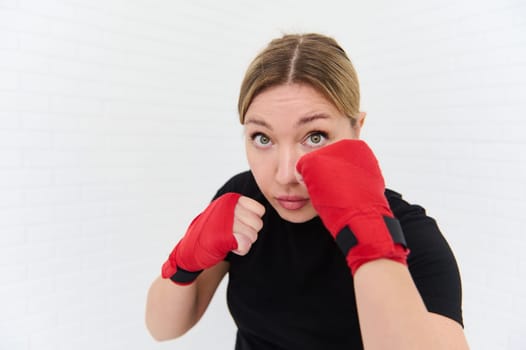 European active professional sport young woman exercising over white background. Attractive athlete sportswoman punching to sand bag to maintain strong muscle for health care. Martial art concept.