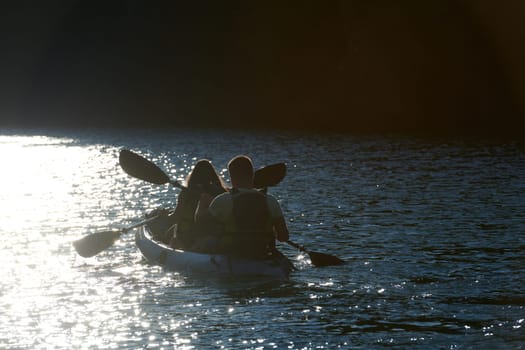 A young couple enjoying an idyllic kayak ride in the middle of a beautiful river surrounded by forest greenery in sunset time.