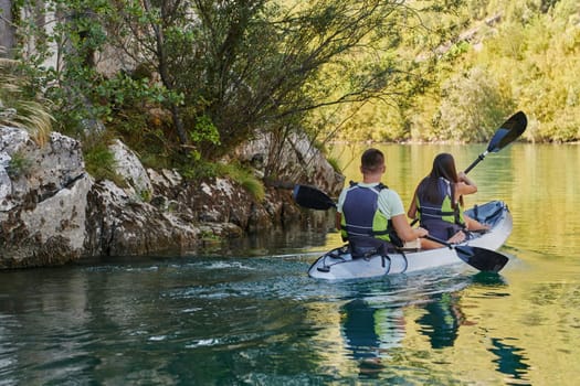 A young couple enjoying an idyllic kayak ride in the middle of a beautiful river surrounded by forest greenery.