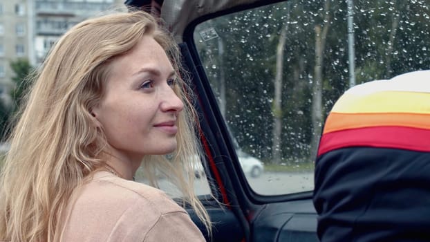 Young woman on passenger seat in a cabriolet car. Stock. Rain drops on car windshield and summer city on the background