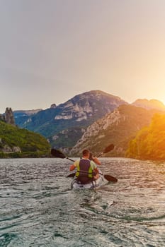 A young couple enjoying an idyllic kayak ride in the middle of a beautiful river surrounded by forest greenery in sunset time.