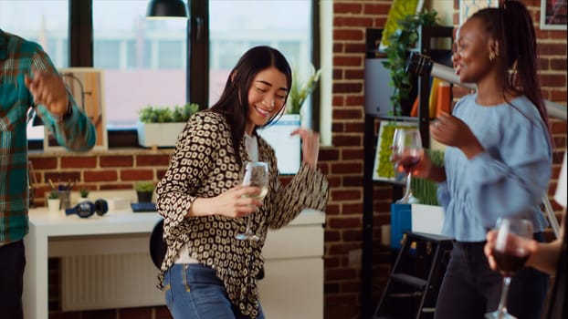 Asian woman doing skillful choreography next to smiling friends dancing at apartment party, entertaining themselves, feeling the rhythm. Colleagues doing energetic dance moves on animated songs