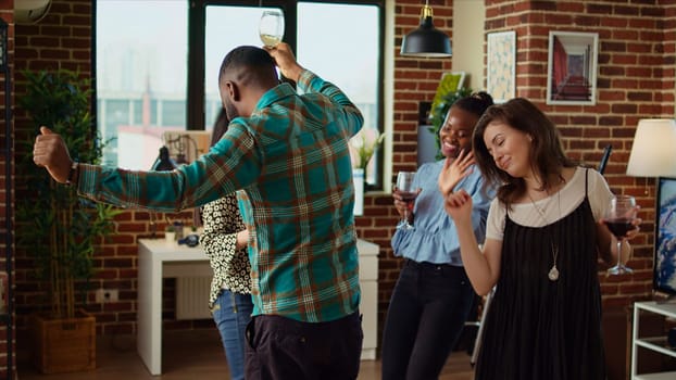 Young adults of various nationalities dancing at home party while drinking alcohol. Friends hanging around, having good time together while enjoying upbeat music in living room