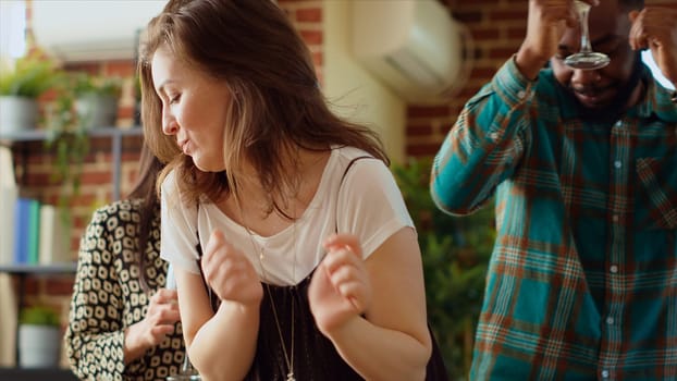 Guests at home party doing dance moves on pop music in living room, holding alcoholic beverages in hand. Group of people dancing on energetic beats during weekend hangout, shaking hips