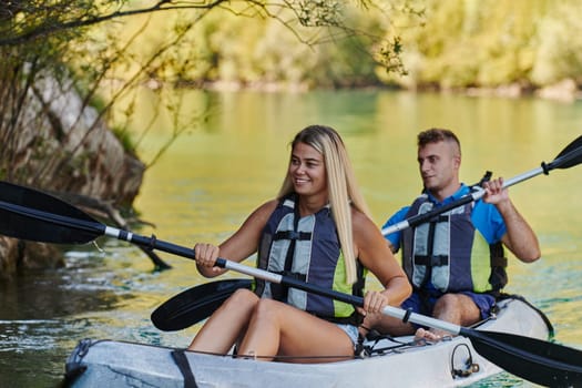 A young couple enjoying an idyllic kayak ride in the middle of a beautiful river surrounded by forest greenery.