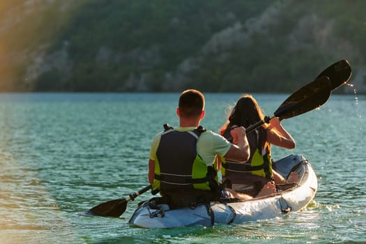 A young couple enjoying an idyllic kayak ride in the middle of a beautiful river surrounded by forest greenery in sunset time.