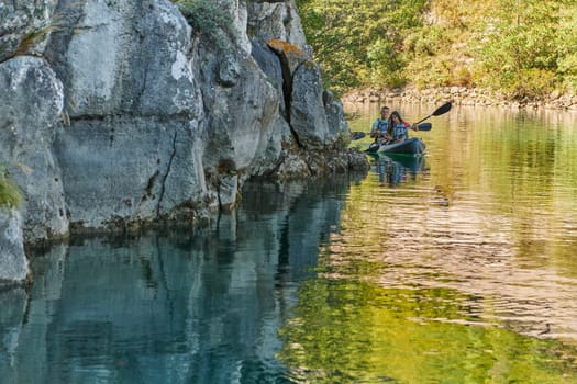 A young couple enjoying an idyllic kayak ride in the middle of a beautiful river surrounded by forest greenery.