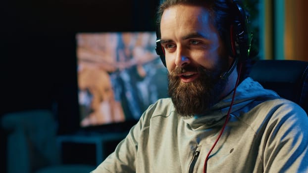 Smiling gamer discussing with teammates while playing competitive esports tournament. Happy man enjoying time spent together with friends in multiplayer videogame, chatting through headset mic