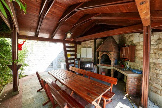 Tables and benches in a wooden gazebo with a stove and kitchen cabinets. High quality photo