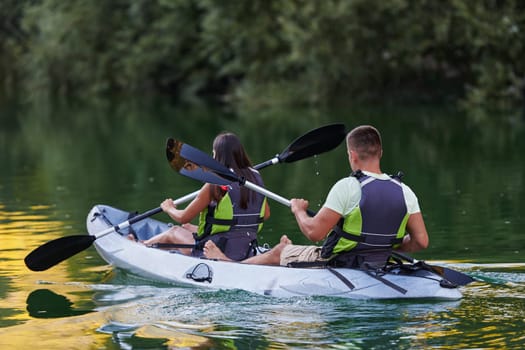 A young couple enjoying an idyllic kayak ride in the middle of a beautiful river surrounded by forest greenery.