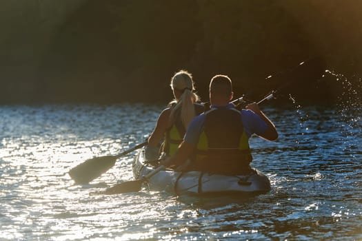 A young couple enjoying an idyllic kayak ride in the middle of a beautiful river surrounded by forest greenery in sunset time.