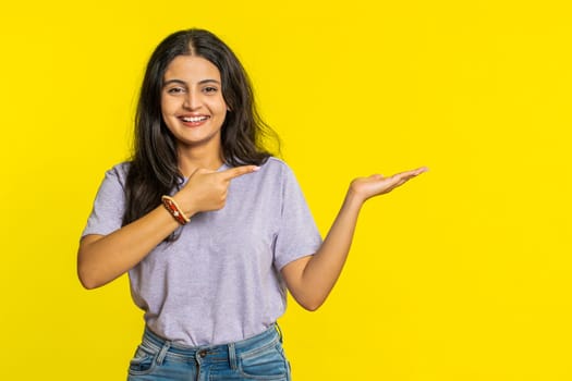 Indian woman showing thumbs up and pointing right empty place, advertising area for commercial text copy space for goods promotion advertisement. Hindu girl isolated on yellow background. Lifestyles