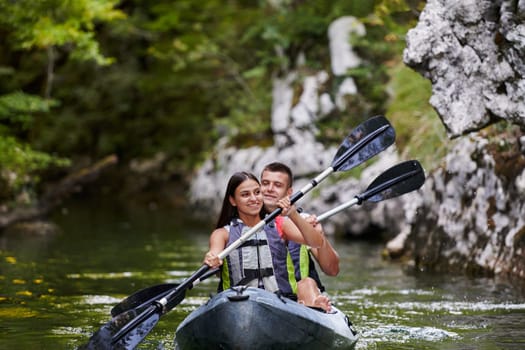 A young couple enjoying an idyllic kayak ride in the middle of a beautiful river surrounded by forest greenery.