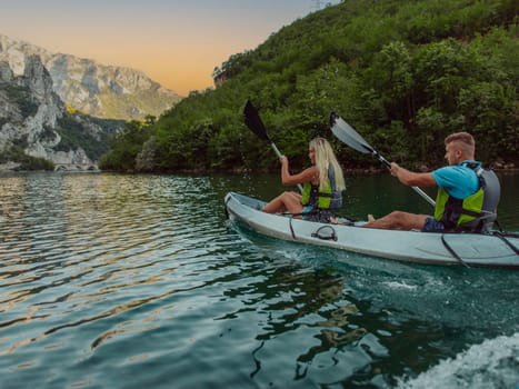 A young couple enjoying an idyllic kayak ride in the middle of a beautiful river surrounded by forest greenery.