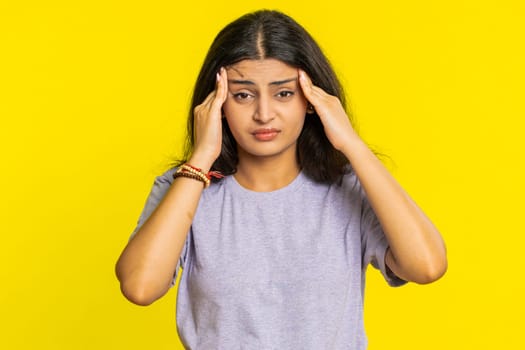Displeased exhausted Indian Hindu woman girl rubbing temples to cure headache problem, suffering from tension, migraine, stress, grimacing in pain, high blood pressure isolated on yellow background