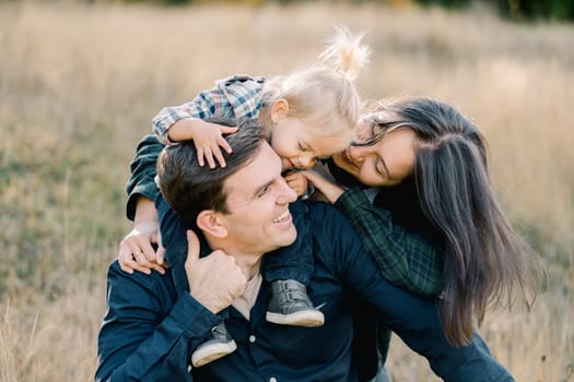 Smiling dad turned his head to mom embracing him and little daughter sitting on his shoulders. High quality photo