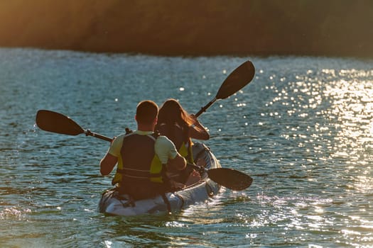 A young couple enjoying an idyllic kayak ride in the middle of a beautiful river surrounded by forest greenery in sunset time.