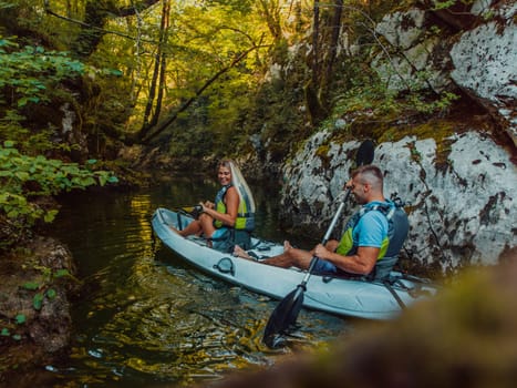 A young couple enjoying an idyllic kayak ride in the middle of a beautiful river surrounded by forest greenery.