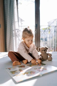 Little girl looks at pictures in a book sitting on the bed. High quality photo