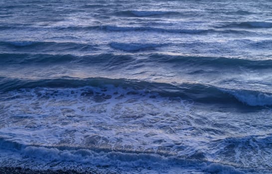 Rippled surface of blue sea water in sunset, orange and teal tones, selective focus