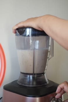 A person is using a kitchen appliance to make a fluid drink. They are blending food, water, and other ingredients to create a smoothie