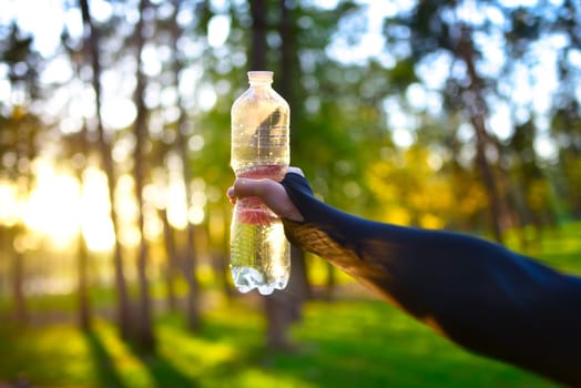 Woman in black sportswear holding a plastic water bottle. Hydration during an outdoor workout. Hidration