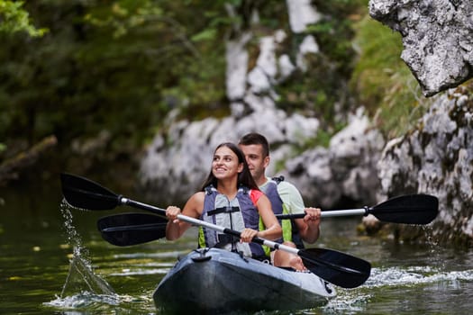 A young couple enjoying an idyllic kayak ride in the middle of a beautiful river surrounded by forest greenery.