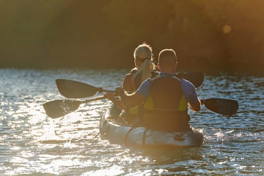 A young couple enjoying an idyllic kayak ride in the middle of a beautiful river surrounded by forest greenery in sunset time.