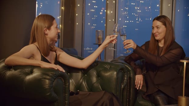 Two beautiful stylish young girls meeting at bar, restaurant, talking, drinking and having fun. Media. Women clinking glasses with champagne